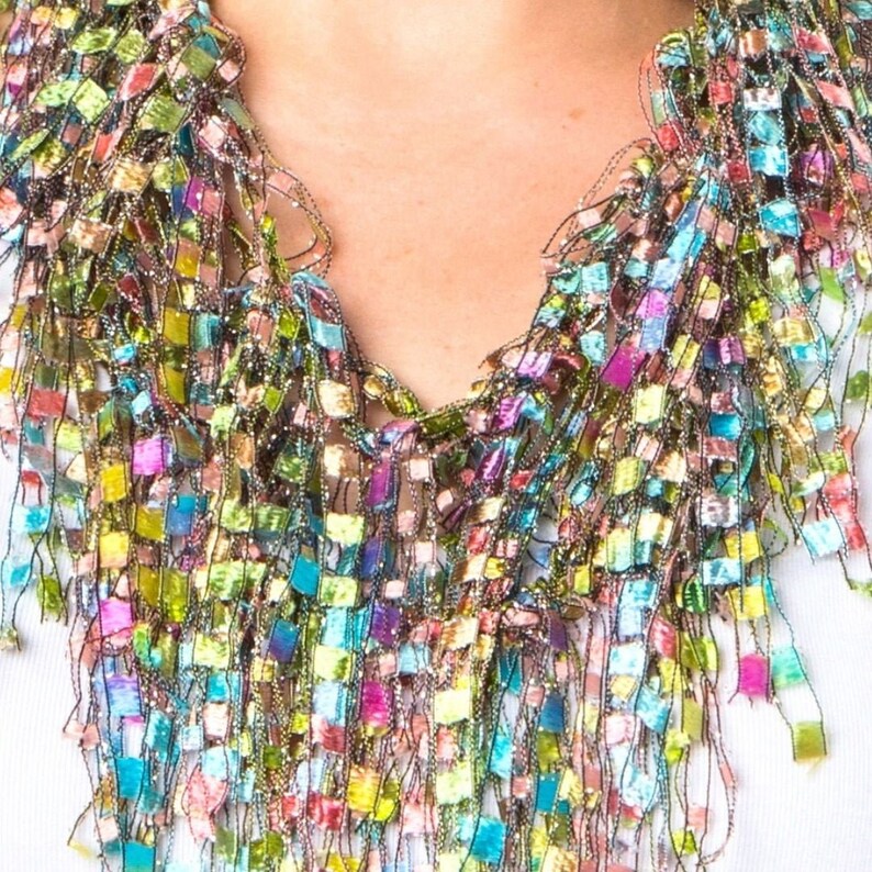 May include: A colorful, multi-layered scarf made of iridescent ribbon. The scarf is made of many small squares of ribbon, creating a fringe effect. The scarf is a vibrant mix of pink, green, blue, and purple.