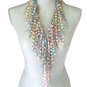May include: A multi-colored crocheted scarf with a fringe design. The scarf is made of a soft, lightweight yarn and features a variety of colors, including pink, blue, green, and yellow.