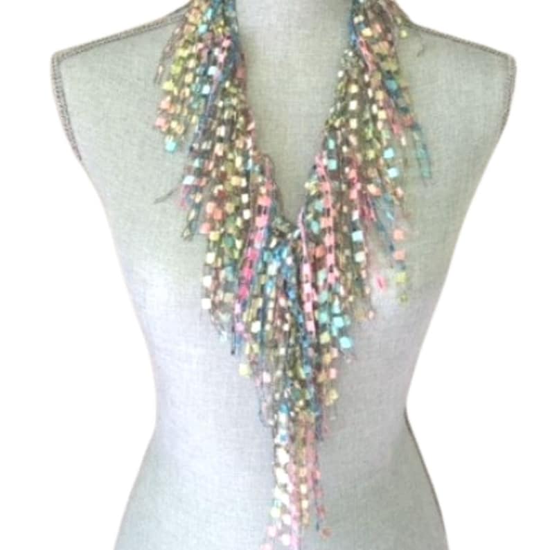 May include: A multi-colored crocheted scarf with a fringe design. The scarf is made of a soft, lightweight yarn and features a variety of colors, including pink, blue, green, and yellow.