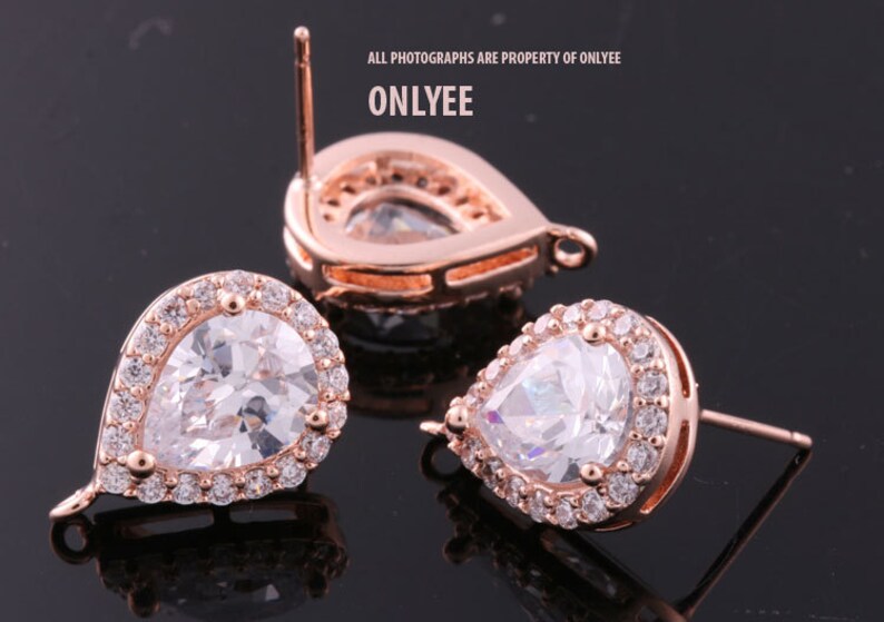 May include: A pair of rose gold teardrop earrings with clear cubic zirconia stones. The earrings have a halo setting and a post back.