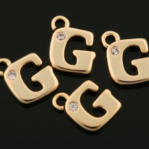 Puede incluir: Cuatro colgantes dorados con la letra "G" y un pequeño acento de cristal transparente. Cada colgante tiene un lazo en la parte superior para sujetarlo a la joyería. Los colgantes tienen forma cuadrada y un acabado brillante.