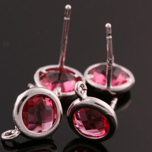 May include: Four silver earrings with pink crystal stones. The earrings have a post back closure.