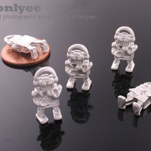 May include: Five silver robot charms with headphones. The robots are standing on a black surface.