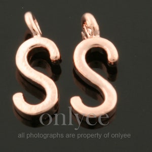May include: Two gold-tone metal letter S charms. The charms are in the shape of the letter S and have a loop at the top for attaching to a necklace or bracelet.