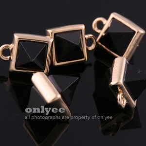 May include: Close-up of several black and gold-colored pyramid-shaped charms. Each charm has a square gold frame and a black, multi-faceted pyramid center. Small loops are attached to the gold frames for stringing or attaching. The text "onlyee" and "all photographs are property of onlyee" is visible.