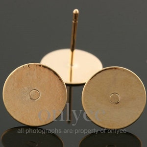May include: Two gold-toned earring posts with round, flat tops. The posts are made of metal and have a smooth finish.