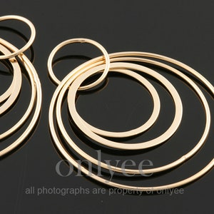 May include: Gold-toned hoop earrings with multiple concentric circles. The earrings are large and have a modern, minimalist design.