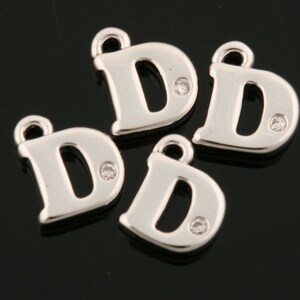 Könnte beinhalten: Vier silberne Anhänger in Form des Buchstabens D, jeder mit einem kleinen, klaren Strassstein in der Mitte.