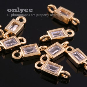 Op de afbeelding: Gouden metalen connector charms met heldere rechthoekige kristal accenten. Elke charm heeft twee lussen om aan sieraden te bevestigen.