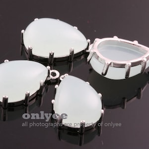 Puede incluir: Tres colgantes en forma de lágrima de color plateado con piedras de cristal transparente. Los ajustes tienen un borde festoneado y un bucle en la parte superior para sujetar una cadena.