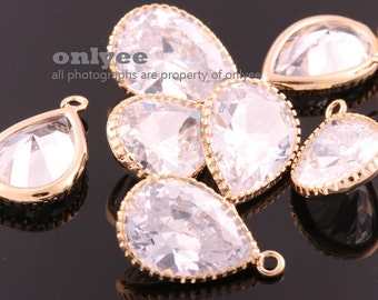 May include: A group of clear teardrop-shaped crystal pendants with gold-toned metal settings. The pendants have a beaded edge and a loop at the top for hanging.
