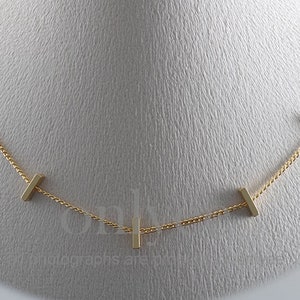 Puede incluir: Un collar de cadena de oro con pequeñas barras rectangulares de oro que cuelgan de él.