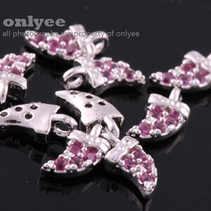 May include: A set of silver-toned charms with pink crystal accents. The charms are shaped like crescent moons and have a detailed design.  "onlyee all photographs are property of onlyee" is printed on the image.