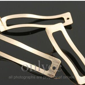 May include: Two gold-toned metal earring blanks with a rectangular shape and a textured finish. The blanks have a hole at the top for attaching an earring post and a smaller hole at the bottom for attaching a charm or other embellishment.