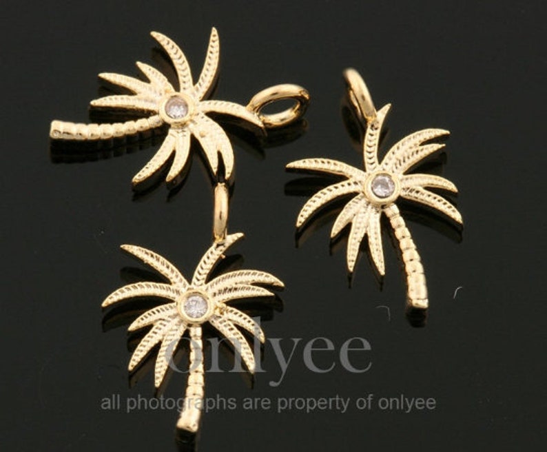May include: Three gold palm tree charms with a clear rhinestone in the center of each tree. The charms have a detailed design and are perfect for jewelry making.