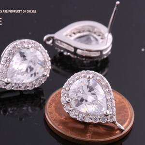 May include: A pair of silver teardrop earrings with clear cubic zirconia stones. The earrings are approximately the size of a US penny.