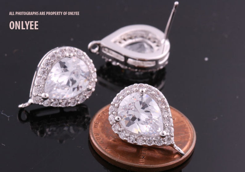 May include: A pair of silver teardrop earrings with clear cubic zirconia stones. The earrings are approximately the size of a US penny.