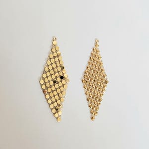 May include: A pair of gold-toned dangle earrings with a diamond-shaped design. The earrings are made of small, interconnected metal circles.