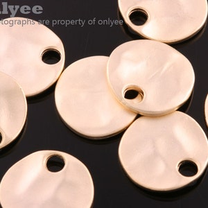 May include: A group of eight gold-colored metal round charms with a hole in the center. The charms have a textured surface and are scattered on a black background.