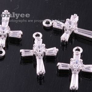 May include: Four silver cross charms with clear crystal accents. Each charm has a loop at the top for attaching to a necklace or bracelet.