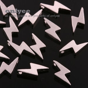 May include: A group of silver-colored lightning bolt charms with a hole in the center for stringing. The charms are scattered on a black surface.