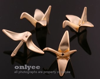 May include: Four gold origami cranes, each folded in a different position, are displayed on a black surface. The cranes are made of metal and have a shiny finish.