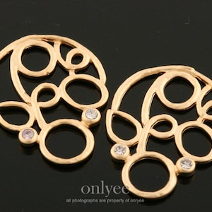 May include: A pair of gold-tone earrings with a delicate, intricate design featuring multiple circles and swirls. Each earring has four small, clear rhinestones.