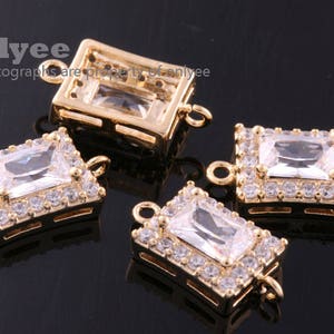 Op de afbeelding: Vier goudkleurige metalen connector charms met heldere zirkonia stenen. Elke charm heeft een rechthoekige vorm met een heldere steen in het midden en kleinere stenen rondom de omtrek.