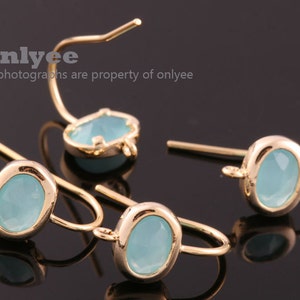 Puede incluir: Tres ganchos de pendientes dorados con piedras ovaladas de color azul claro. Las piedras están engastadas en un marco de metal dorado.