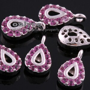 May include: Six silver teardrop-shaped charms with pink rhinestone accents. Each charm has a loop at the top for attaching to jewelry.