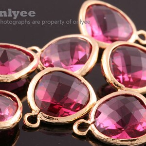 May include: A group of seven pink glass teardrop-shaped charms with gold-toned metal settings. Each charm has a small loop at the top for attaching to jewelry.
