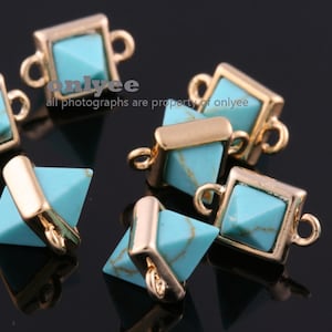 May include: Gold-tone metal connector charms with turquoise blue gemstone accents. The charms are shaped like squares and pyramids.