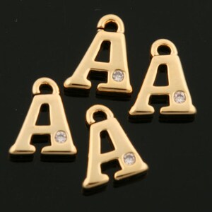 Puede incluir: Cuatro abalorios de letras A doradas con un brillante transparente en el centro de cada letra. Los abalorios tienen un bucle en la parte superior para sujetarlos a joyas.
