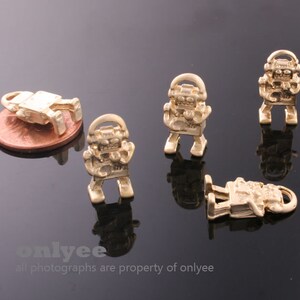 May include: Five gold-colored robot charms, each with a different pose. The charms are small and detailed, with a shiny finish.