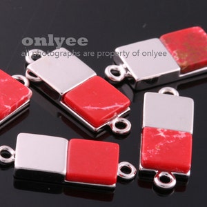 Pode incluir: Cinco conectores quadrados de cor prateada e vermelha com dois laços em cada um. Os conectores são feitos de metal e têm uma incrustação de pedra vermelha.