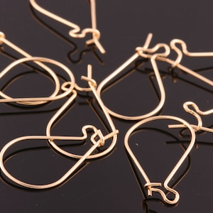 May include: A close-up of a group of gold-toned earring hooks. The hooks are made of metal and have a teardrop shape.