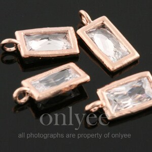 Op de afbeelding: Vier rechthoekige bedels in rosé-goud met heldere kristallen accenten. Elke bedel heeft een kleine lus aan de bovenkant om aan sieraden te bevestigen.