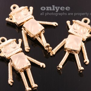 May include: Three gold robot charms with a detailed design. The charms have a loop at the top for attaching to a necklace or bracelet.