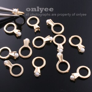 May include: A group of 12 gold-tone ring charms with a pearl accent. The charms are arranged on a black surface.