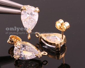 May include: Two gold-tone teardrop-shaped earring findings with clear cubic zirconia stones. Each finding has a loop at the top for attaching a dangle earring.