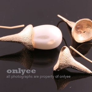 May include: Gold-toned earrings with a textured, bell-shaped design and a white, oval-shaped pearl. The earrings have a hook closure. The image also includes the text "onlyee" and "all photographs are property of onlyee".