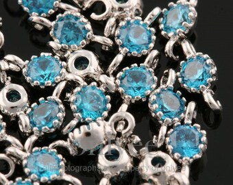 May include: A close-up of silver-toned metal charms with blue crystal accents. The charms have a loop at the top for attaching to a bracelet or necklace.
