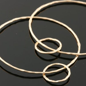 May include: Close-up of several gold-colored hoop earrings with a hammered texture. The earrings are arranged in a cluster, with varying sizes of circular shapes. The background is a dark, reflective surface.