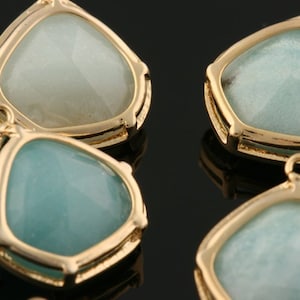 Puede incluir: Cuatro colgantes de tono dorado con forma de lágrima y una piedra de vidrio azul claro o blanca en el centro.