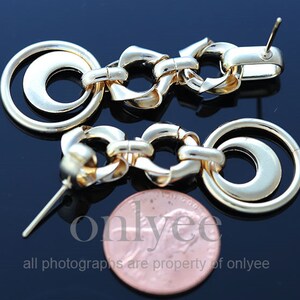 May include: A pair of gold-tone earrings with a chain link design and a double circle pendant. The earrings are approximately 2 inches long.