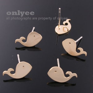 May include: Four gold-colored whale stud earrings. Each earring features a whale silhouette with a small tail fin. The earrings are on a black background.