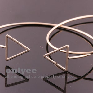 Può includere: Tre braccialetti rigidi dorati a forma di triangolo. I braccialetti sono semplici e minimalisti, con un design delicato a forma di triangolo.