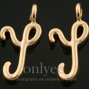 May include: Two gold-colored metal charms in the shape of the letter 'y' with a cursive script font. The charms have a loop at the top for attaching to a necklace or bracelet.