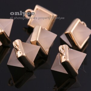 May include: Five gold-toned pyramid-shaped charms with a clear, light brown stone in the center. The charms have a loop at the top for attaching to jewelry.