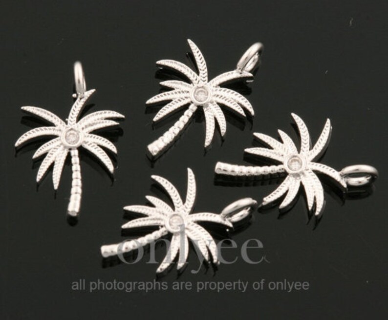 May include: Five silver palm tree charms with clear rhinestone accents. Each charm has a loop for attaching to a necklace or bracelet.
